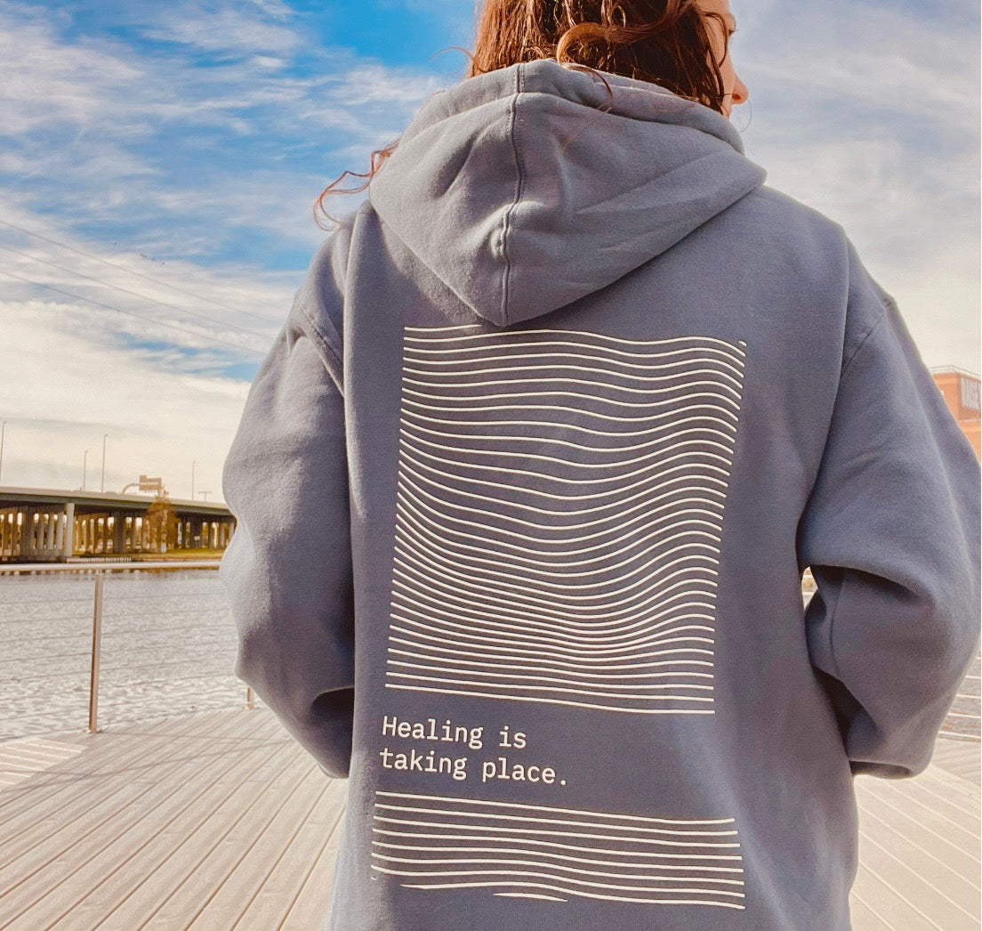 Girl showing the back of a blue hoodie that says "Healing is taking place."